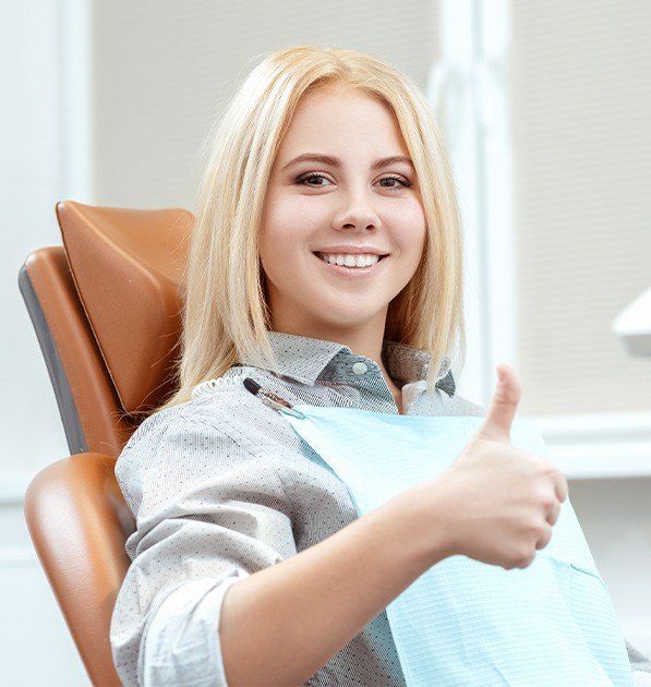 Woman in dental chair giving thumbs up after dentl checkup