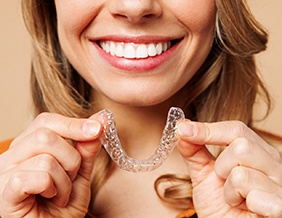 Smiling patient holding clear aligner